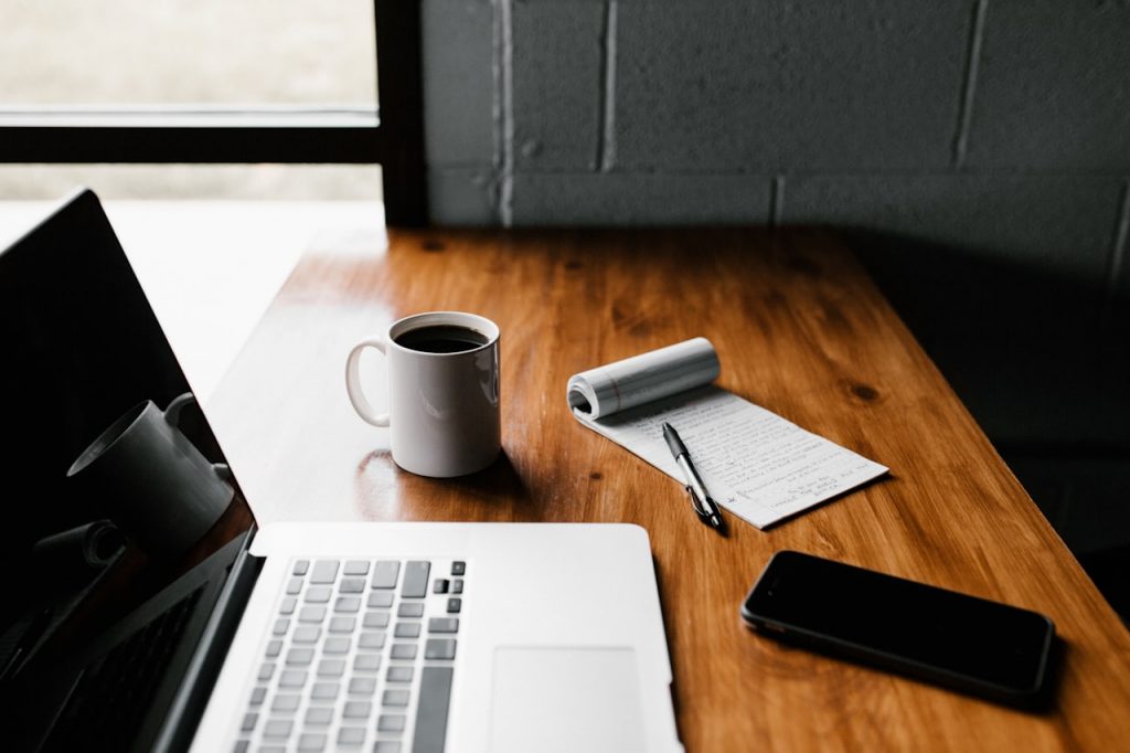 Coffee cup and notebook on a desk next to a laptop – symbolic of professional communication and collaboration at Owtana Tech.
